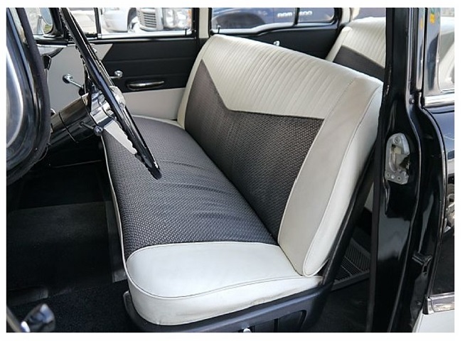 This interior view shows the front seat from the driver's side. The seat and door panels are in matching black and white, floor, dash with instruments, steering column