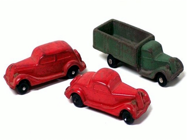 There are three vehicles in this group of Barr vehicles, a red two-door fastback with rear mounted spare and black tires, a red '35 coupe with rear spare and black tires, and a green stake-side, dual-rear wheel truck