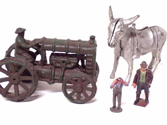 Here we have a cast tractor, possibly based on the Fordson tractor, a 2-part saddled mule, and two cast metal figures, one a country gent in coat and vest with a bowler hat, pants tucked into tall boots, and the other a working fellow in overalls carrying with both arms a heavy bag over his back.