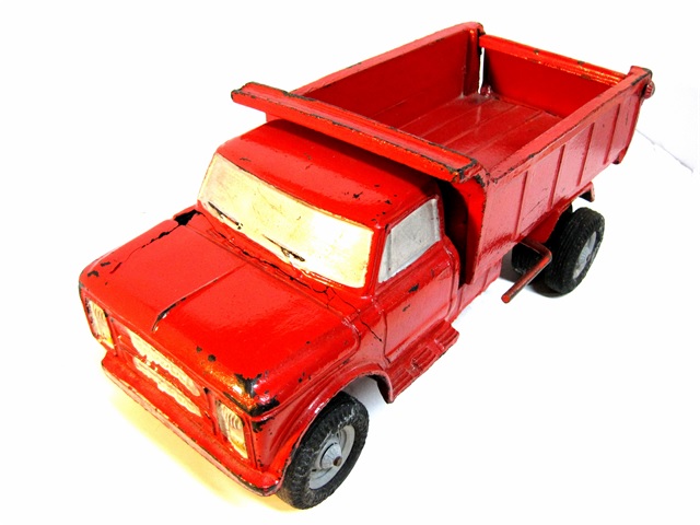 A fine, sturdy truck, in bright red paint. It has a lever operated lift and a working tailgate. Below smallish but functional fenders, there are dual wheels on the back. At the front there are dual headlamps stacked one atop the other between the two wide, rectangular chromed grill openings. There is a large, wide front windscreen, a wide rear windscreen, and a window at each side. There are wing vents on the side as well. Access to the truck is eased by running boards. The two large fuel tanks are attached to frame just behind the cab.