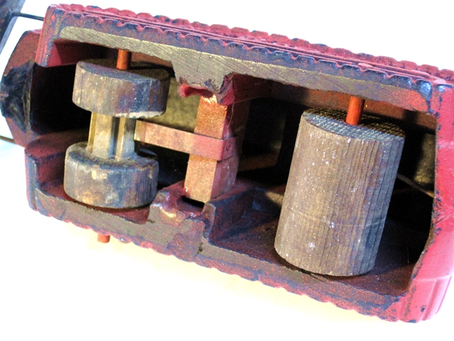 This is the underside of one of the dozers with the noise-maker. The bosses mentioned previously have been channeled so that a rectangle of wood slides into them. attached to it is a thin strip of metal which is long enough to reach the bottom of the channels. As this wheel passes beneath the strip, it clicks loudly.I expect kids really liked it. Parents? Probably not so much.