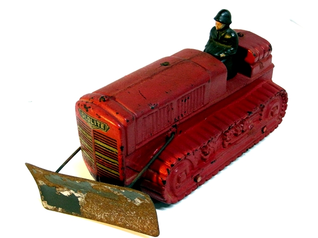 This photo is a front quarter view. The military driver is in seat. The dozer body is dark red and in good condition, the exhaust stack is missing, the blade is missing most of its black paint and is rusty, but the Glolite decal is very good. The metal blade is in very good shape.