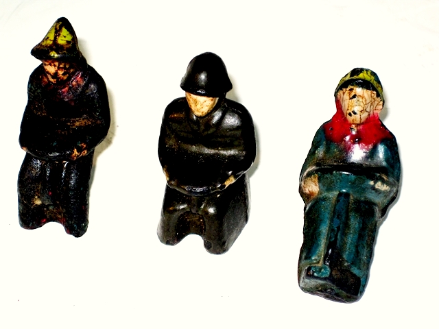 This is a photo of the three drivers for Glolite toys. On the left is a farmer figure with very poor paint for his yellow hat and red kerchief. The rest of the paint has all worn away from this fellow, but another farmer driver has blue apparel.. Next to the farmer is an Army driver who is painted khaki from helmet down, leaving only the beige colored face. The paint is excellent. Last comes another farmer, this one identical to the dozer driver but made so that he will not fit the dozer, only the Jeep. His clothing is like the first, but his paint remains very good. This photo is a frontal view of the three drivers, and shows how the steering wheel missing from the vehicle castings actually is part of the drivers' castings, looking somewhat like a large dinner plate in their laps.