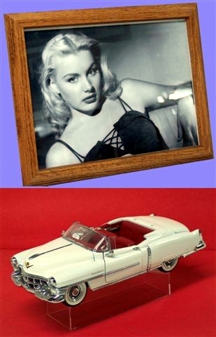 In this picture there is a framed 8x10 photo of the actress Barbara Payton above a white 1:24 scale diecast 1953 Cadillac convertible with red interior.