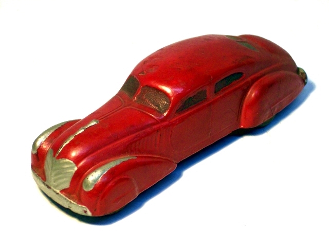 A bright red 1936 Teardrop Sedan viewed from the left front. The windows are black (perhaps inked), and the trim is painted silver. This five and a half inch toy looks like its real-life version could really burn up the highway, which makes the trailer hitch some have a bit odd.
