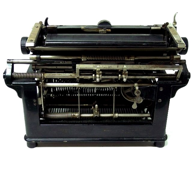 From the rear and slightly above, the back of the carriage is seen with its component parts and carriage rails. The open frame reveals the typebars and makes access somewhat easy. To the right at the back is the large, easily accessible drawband spool and the escapement mechanism. The drawband attaches to a flat casting which in turn attaches to the frame.